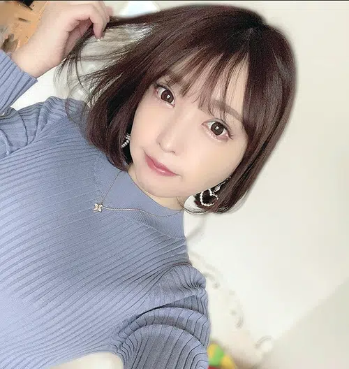 A young Asian woman snaps a selfie of herself. She's wearing a lavender colored sweater. With wide eyes, she looks at you, her free hand plays with her hair.